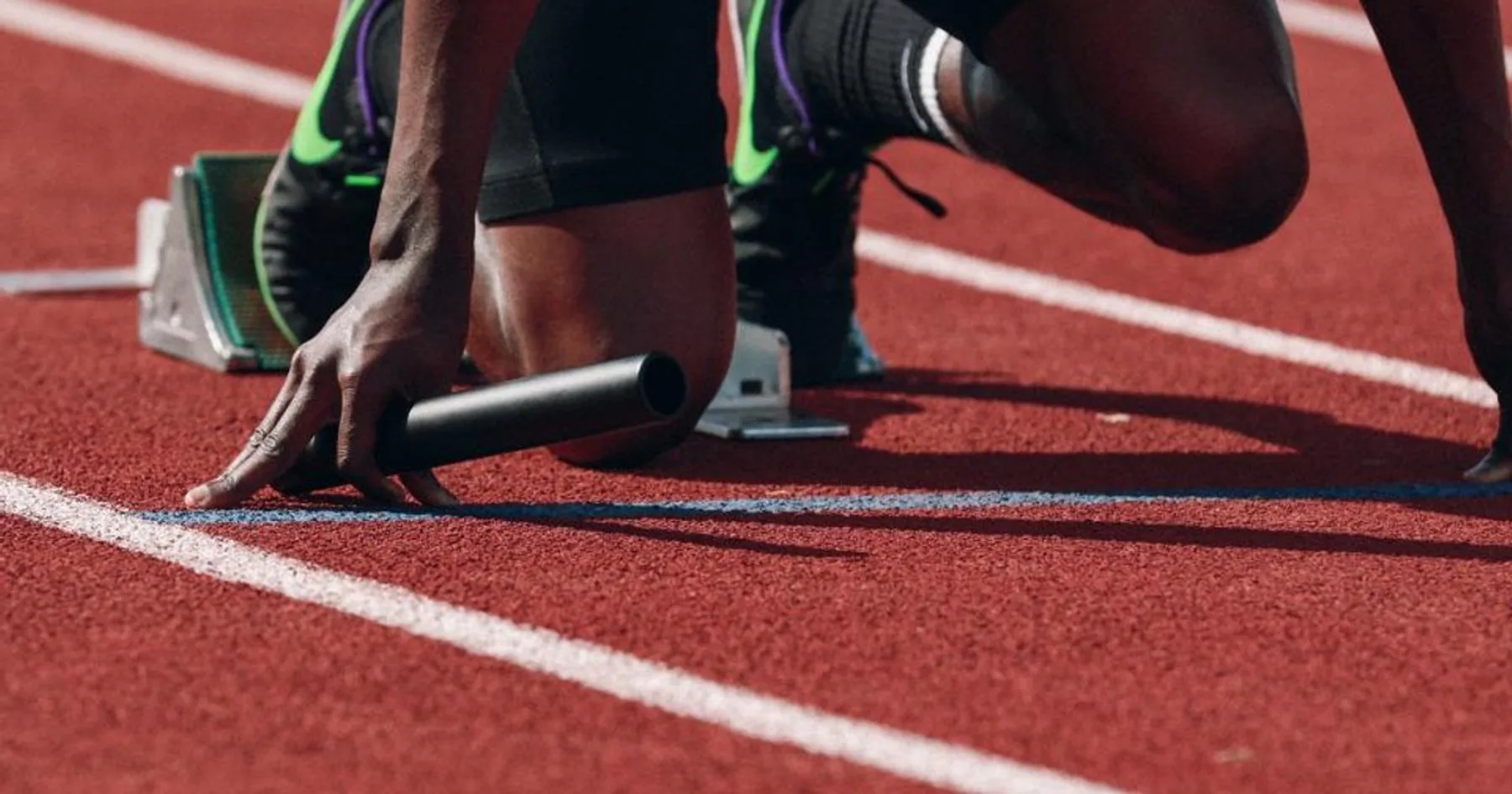 Mãos de velocista apoiadas na linha de largada da pista de atletismo